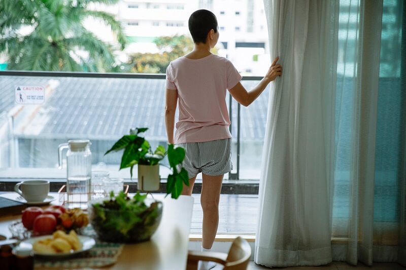 Short haired sick woman opening curtain of window in hospital