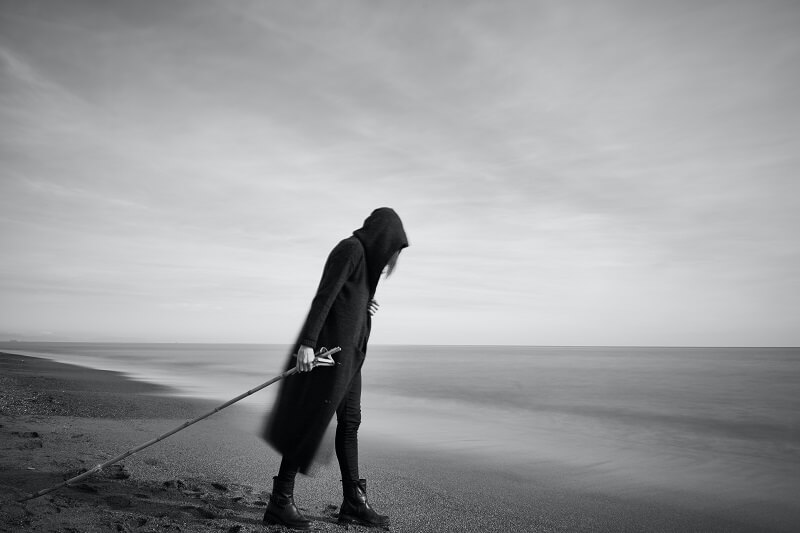 Woman in Black Cloak With Fishing Pole Standing in Beach