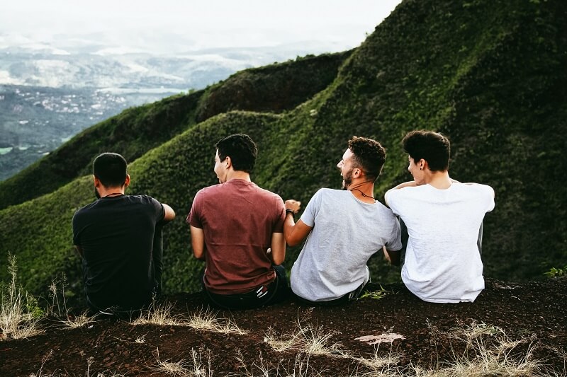 Row of four men sitting on mountain trail